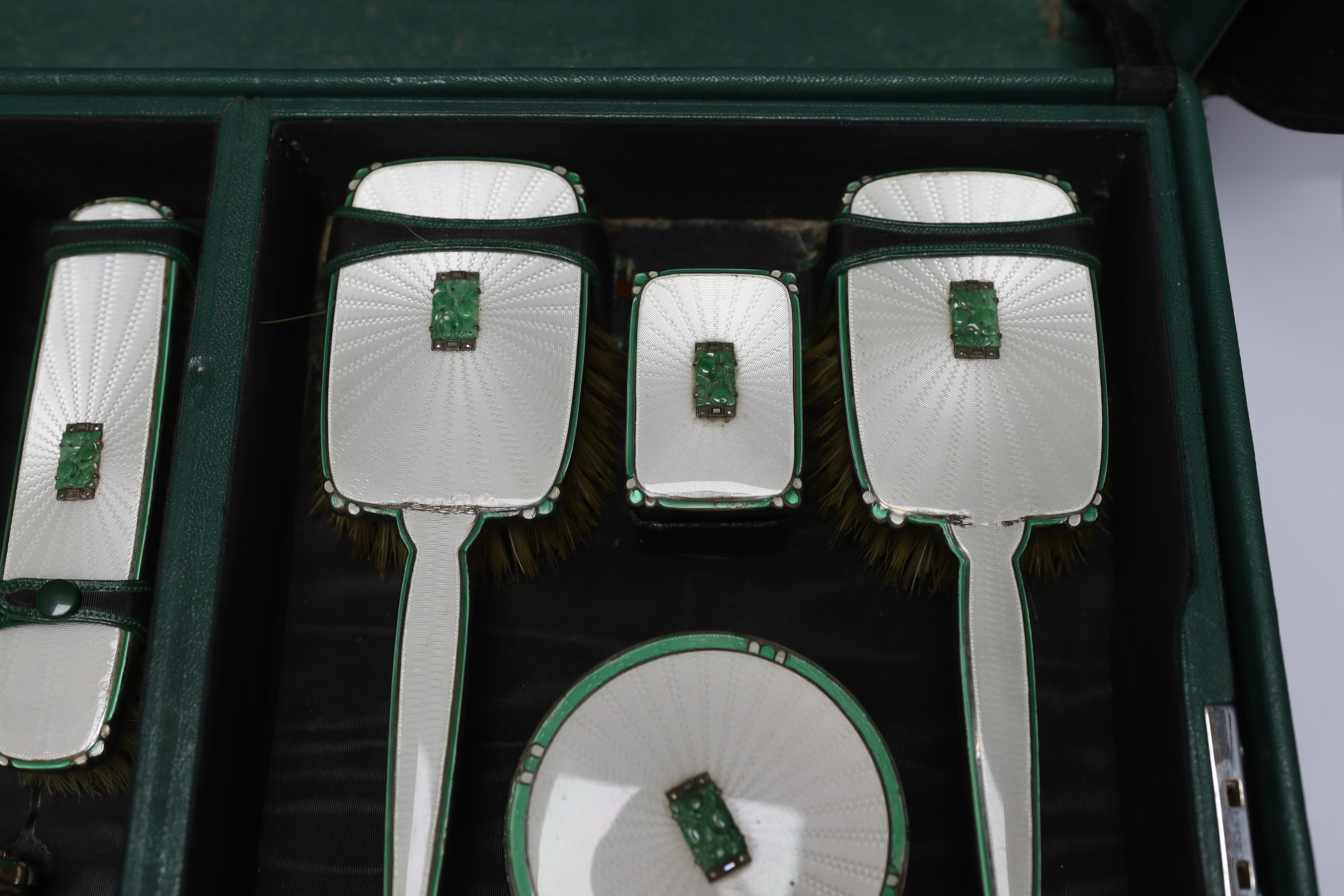 A George V silver, enamel and Chinese jadeite mounted twelve piece dressing table set, Goldsmiths & Silversmiths Co Ltd, Birmingham, 1936, housed in green leather travelling case, case width 53cm (a.f.).